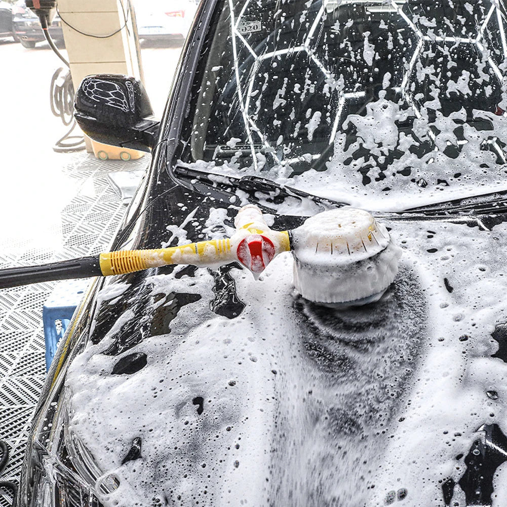 A spinning wash brush working through thick foam on the hood of a black car.