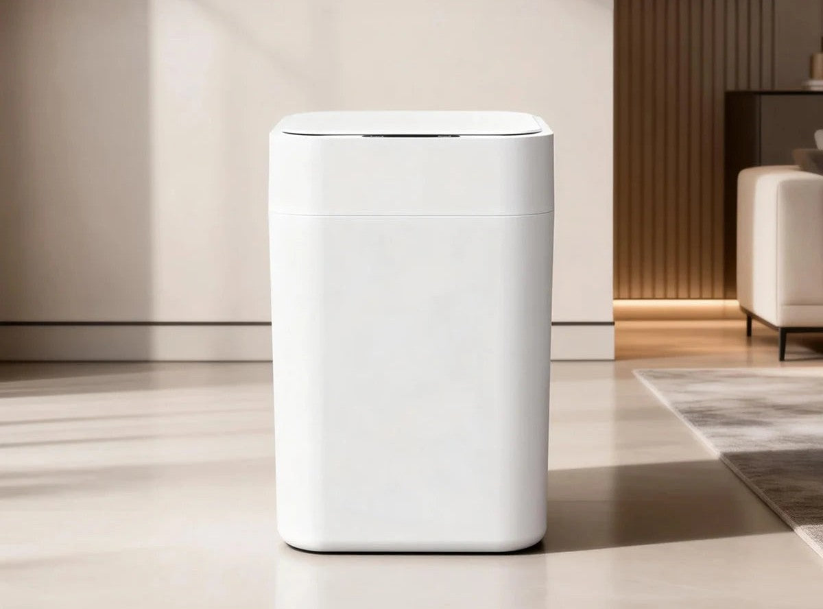 A white touchless smart trash can standing on a pale stone floor in a bright, minimal living room.